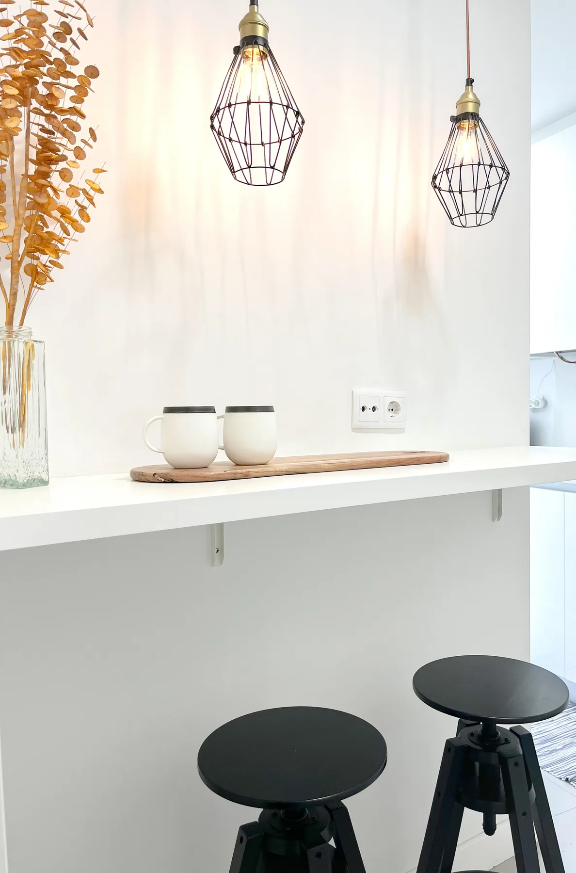A bright kitchen counter with two stools and hanging pendant lights.
