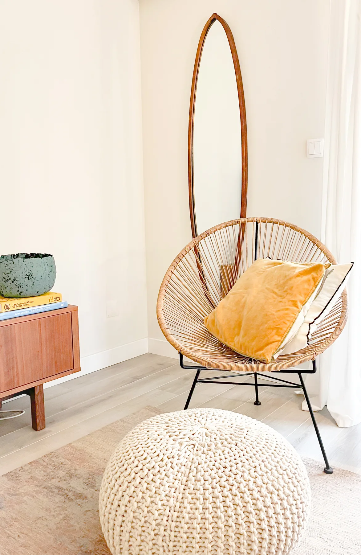 A bright sitting area features a woven lounge chair and a round pouf.
