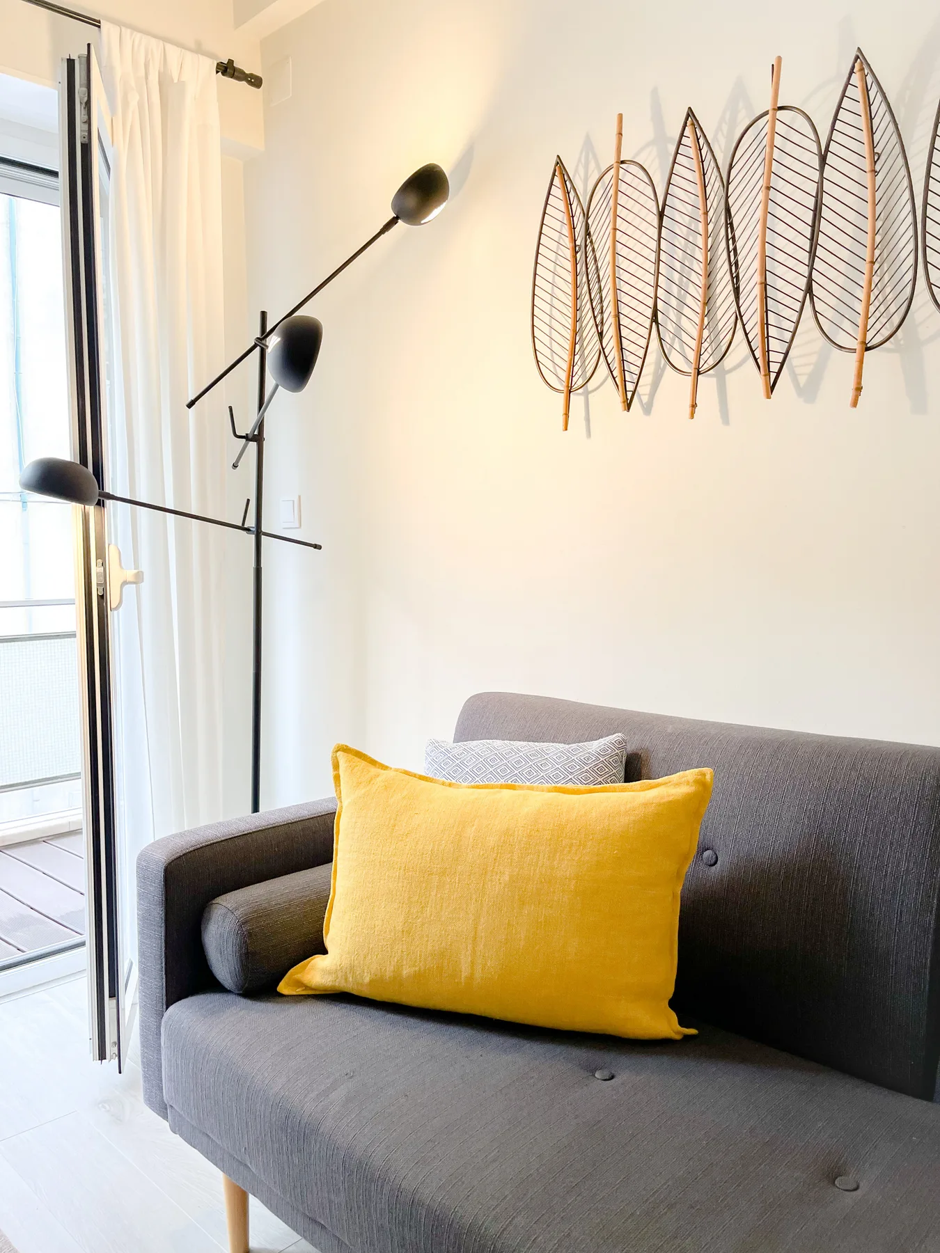 A gray sofa with a yellow cushion sits beside a glass balcony door.