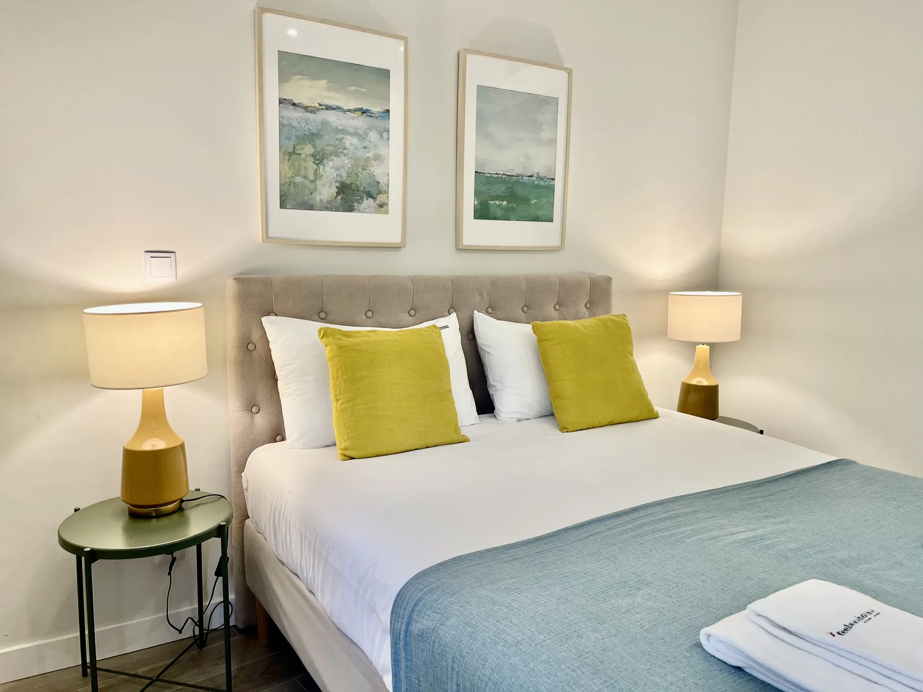 A bedroom with a neatly made bed, colorful cushions, and framed artwork.