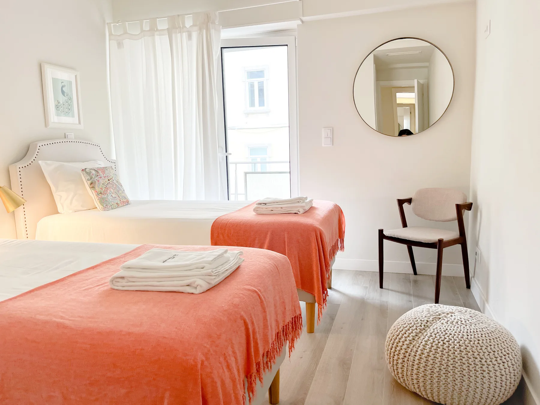 A bright bedroom with two beds and a chair beside the window.