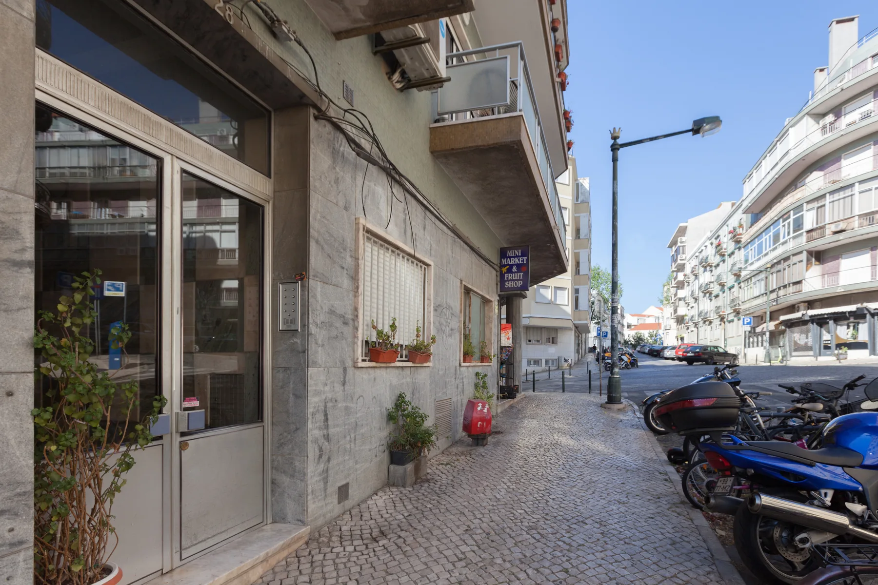 A cobblestone street lined with buildings, parked scooters, and storefronts.