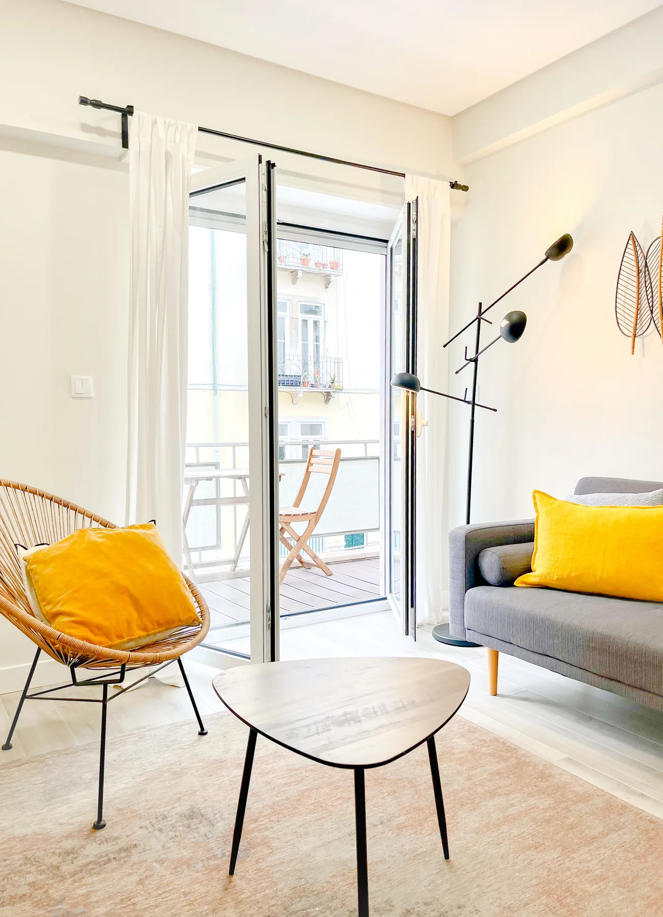 A bright living room with seating beside open glass doors leading to a balcony.