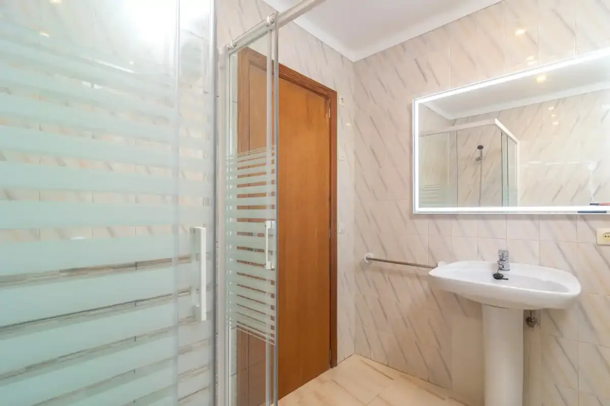 Un baño con lavabo, espejo y panel de ducha de vidrio.