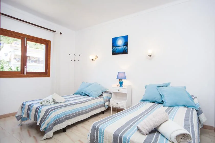Un dormitorio luminoso con dos camas individuales, ropa de cama a rayas y una ventana con marco de madera.