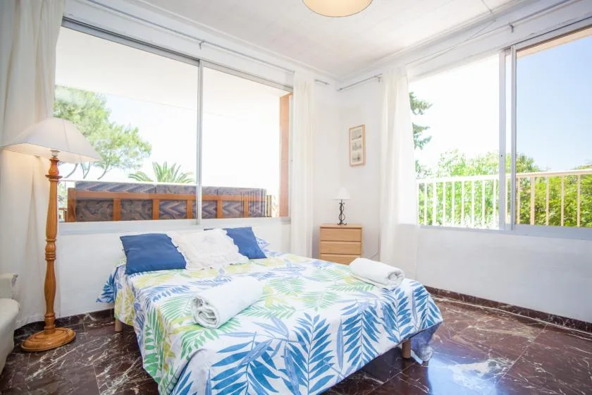 Un dormitorio luminoso con una cama cubierta con ropa de cama estampada con hojas azules y verdes.