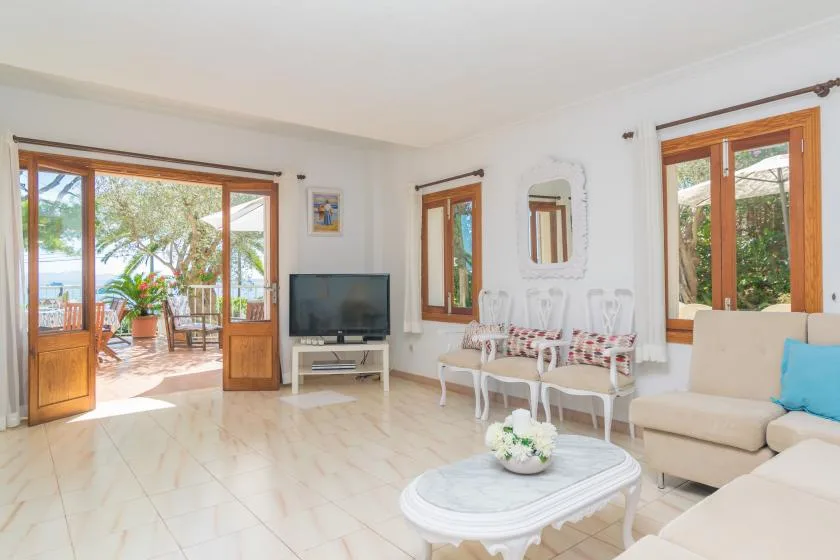 Una luminosa sala de estar con asientos, televisor y puertas que dan a un patio.