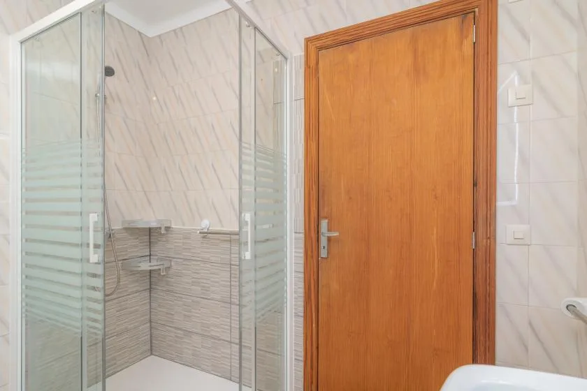 Un baño alicatado con ducha de vidrio y puerta de madera.