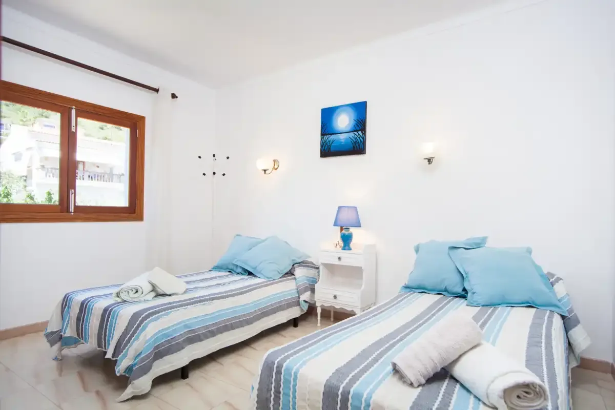 Un dormitorio luminoso tiene dos camas individuales con ropa de cama a rayas junto a una ventana.