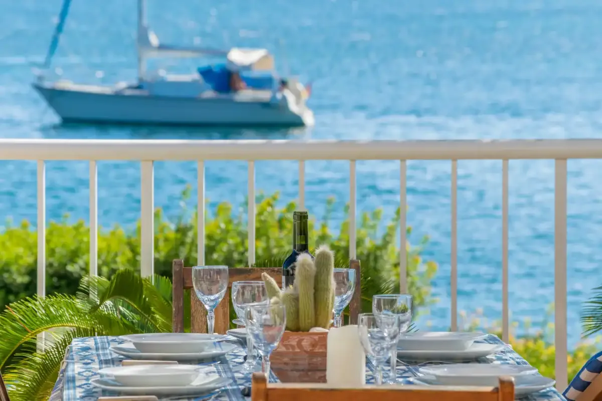 Una mesa de comedor junto al mar está puesta junto a una barandilla con vistas al agua.