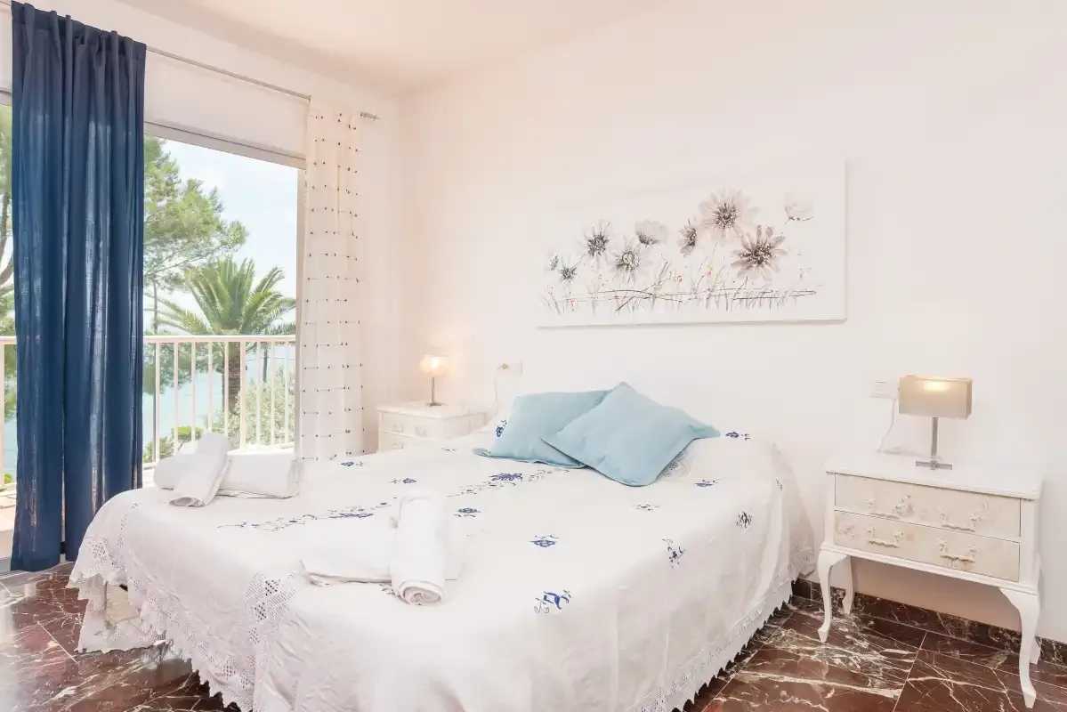 Un dormitorio luminoso con una cama junto a una puerta abierta al balcón.