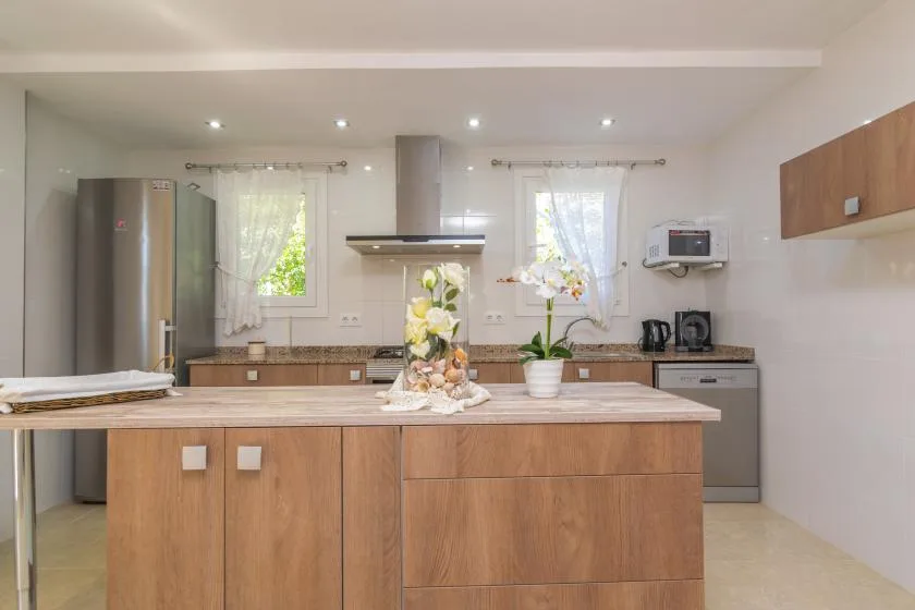 Una cocina luminosa con una isla central, un refrigerador de acero inoxidable y ventanas.