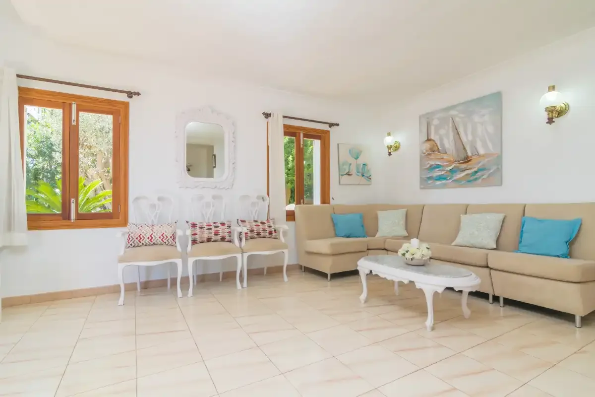 Una sala de estar luminosa con un sofá beige y sillas blancas junto a las ventanas.