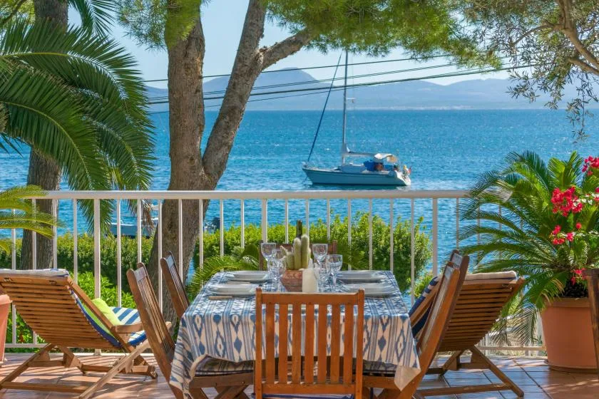 Comedor al aire libre con mesa y asientos frente al mar y un barco.