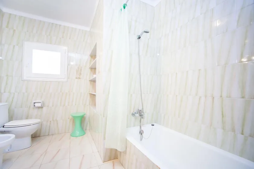 Un baño con azulejos, bañera, ducha, inodoro y una ventana pequeña.