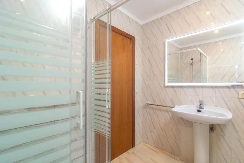 Un baño con lavabo de pedestal, espejo y mampara de ducha de vidrio.
