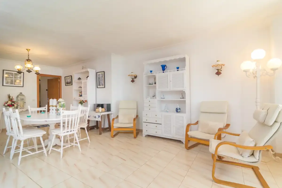 Un luminoso salón comedor con asientos blancos, una mesa de comedor y vitrinas.