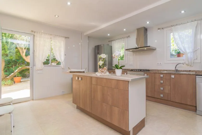 Una cocina luminosa con una isla de frentes de madera y plantas sobre la encimera.