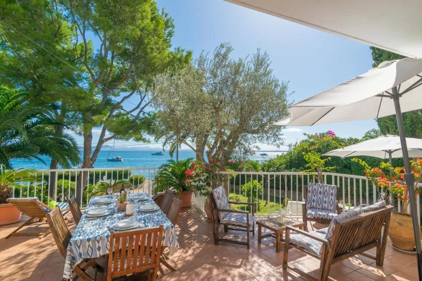 Una terraza junto al mar con asientos al aire libre, mesas, árboles y vistas al agua.