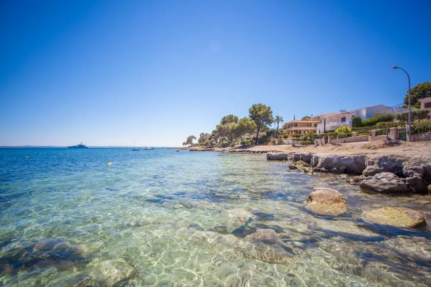 Una costa de aguas poco profundas y claras, con rocas y edificios junto al mar.
