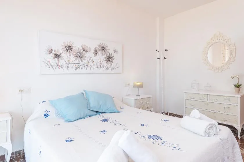 Un dormitorio luminoso con una cama vestida con ropa de cama blanca y azul con flores.