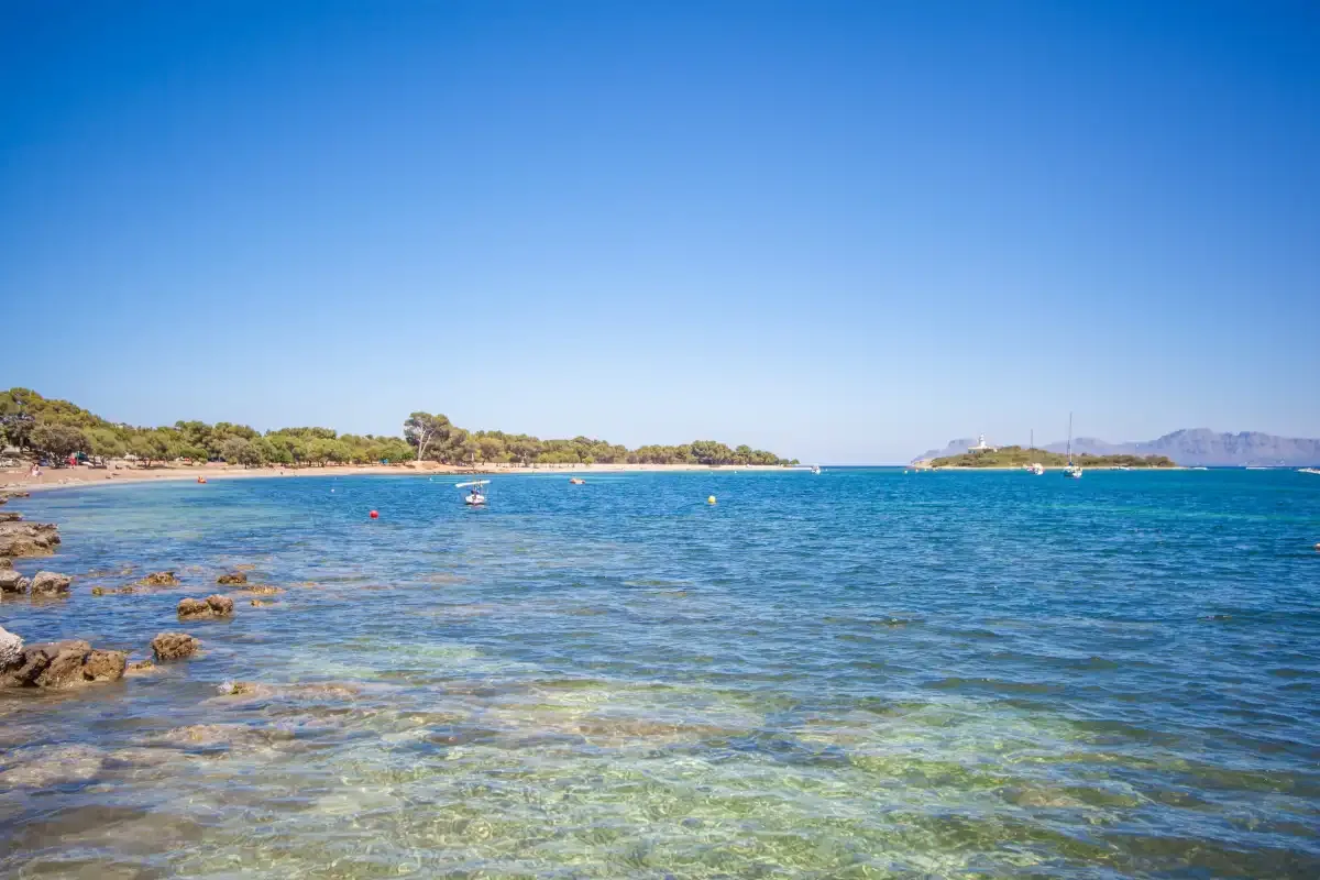 El mar azul y transparente se extiende junto a una costa rocosa bajo un cielo despejado.