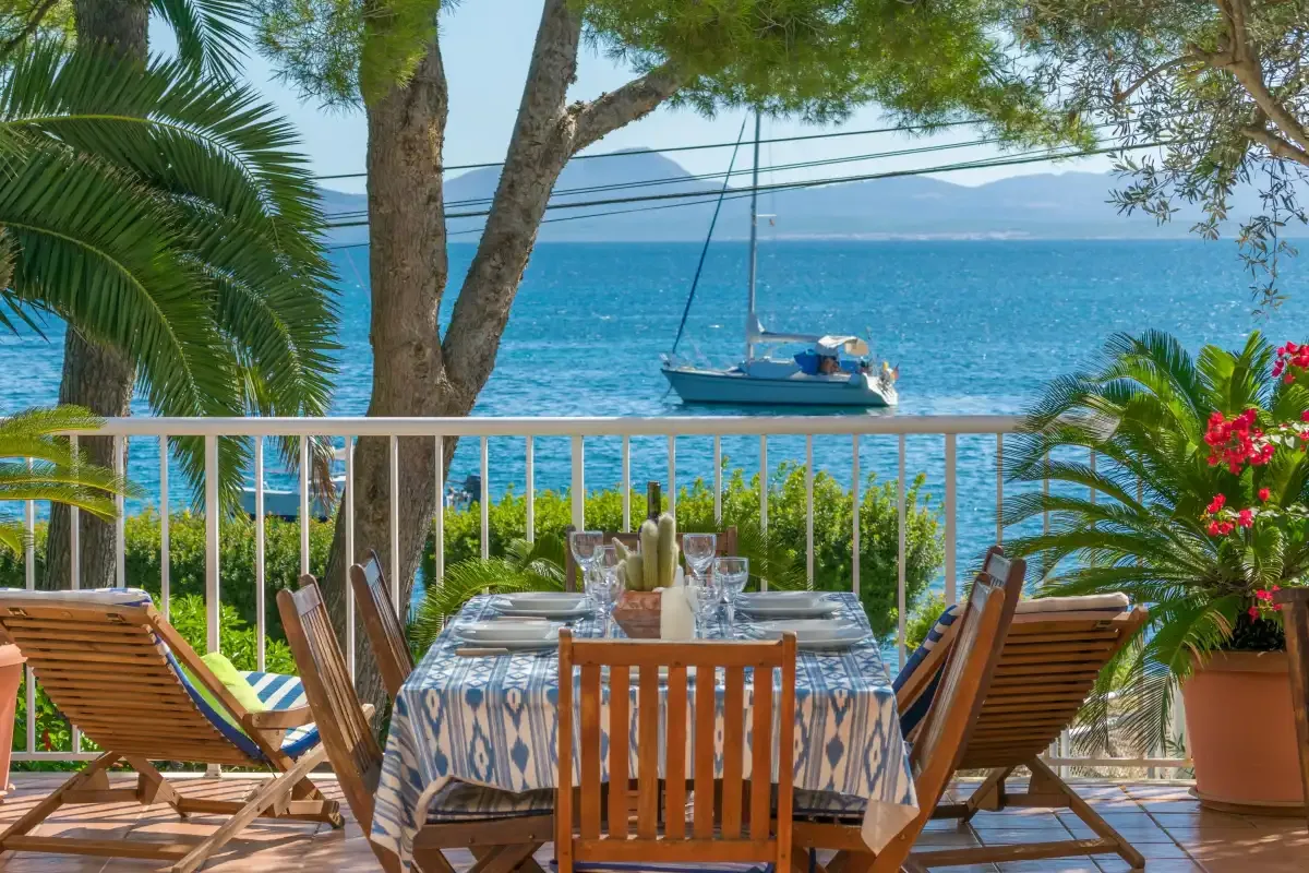 Una terraza junto al mar da al agua, con un velero a lo lejos.