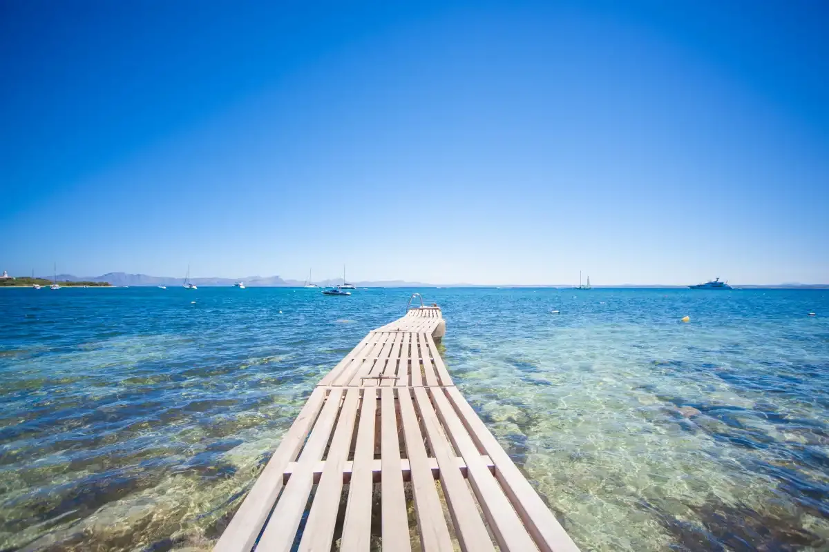 Una pasarela de madera se adentra en aguas claras y poco profundas hacia el mar abierto.