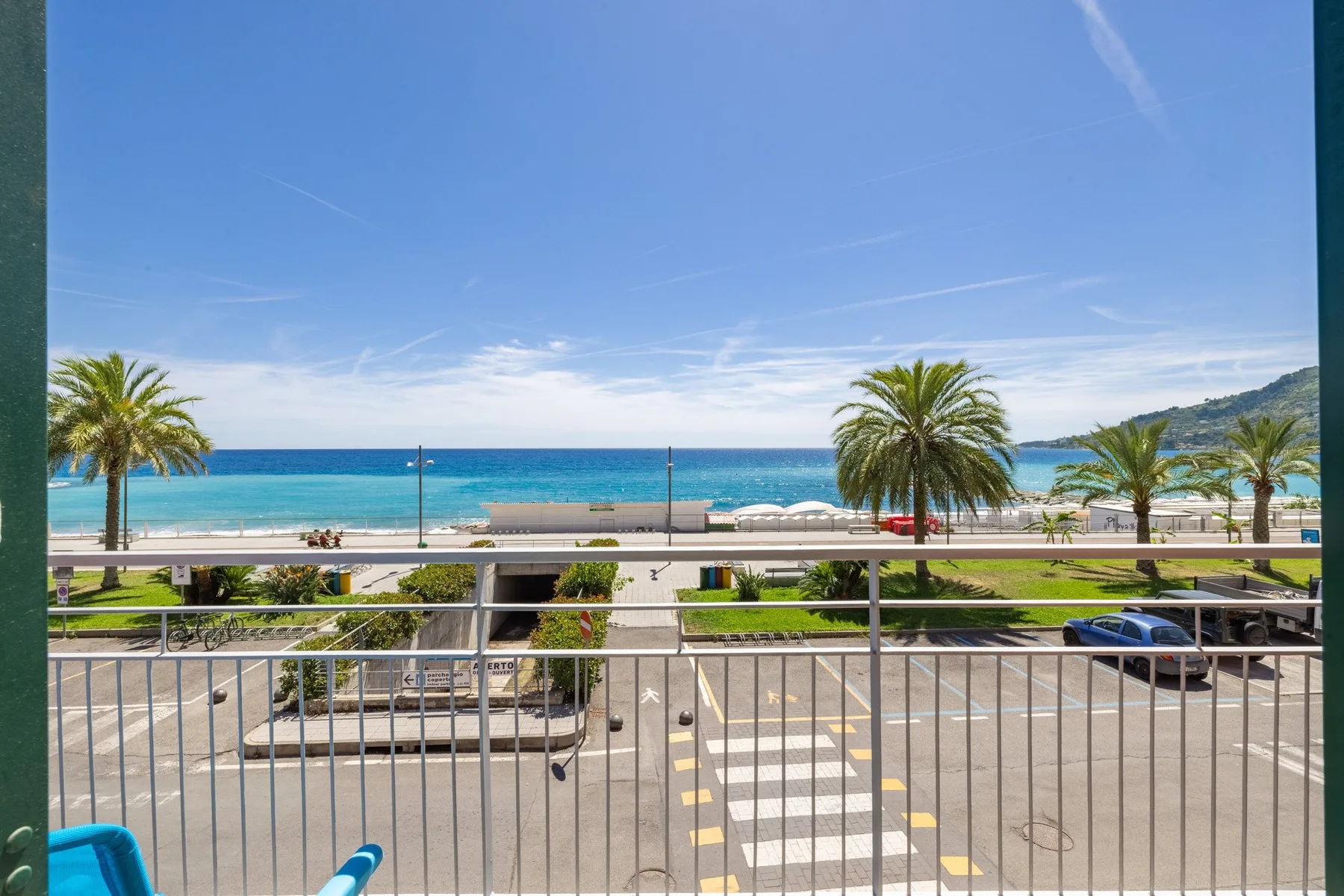 A seaside road and promenade overlook a beach lined with palm trees.