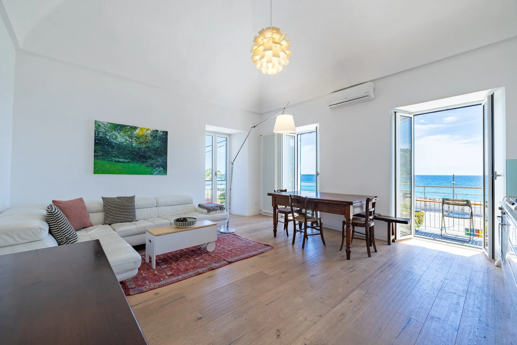 A bright living and dining area opens onto a balcony overlooking the sea.
