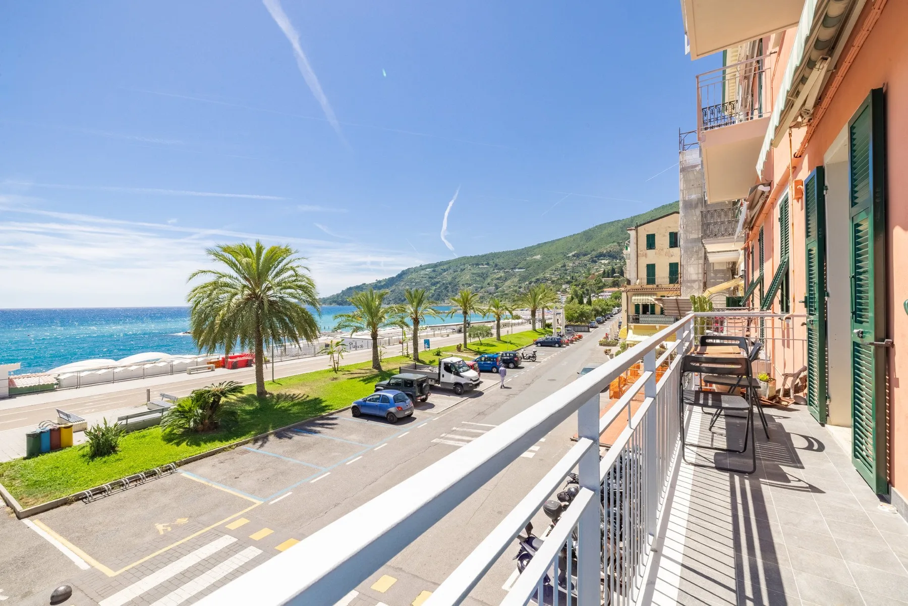 A balcony overlooks a coastal street with palm trees and the sea beyond.