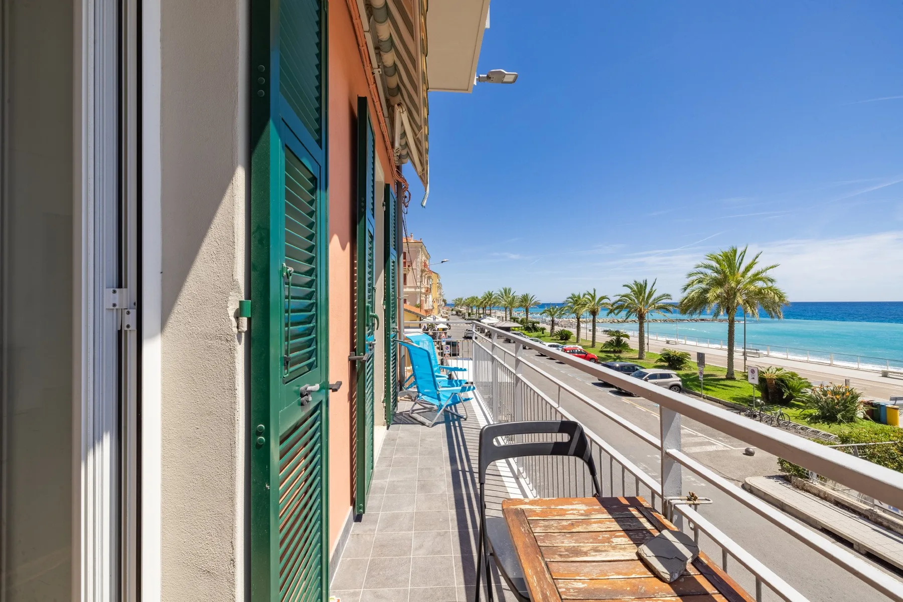 A seaside balcony overlooks palm trees, a promenade, and the ocean.