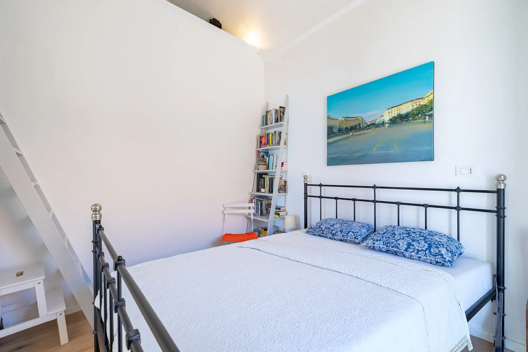 A bright bedroom with a black metal bed and a colorful picture above it.
