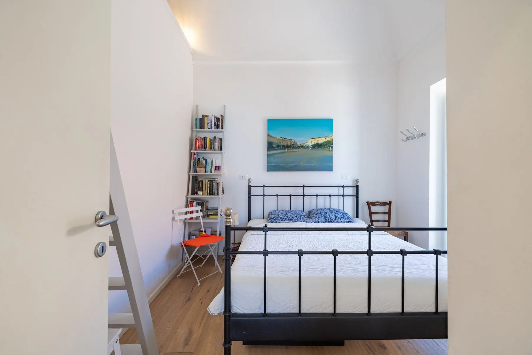 A bright bedroom with a black metal bed and a landscape print above it.