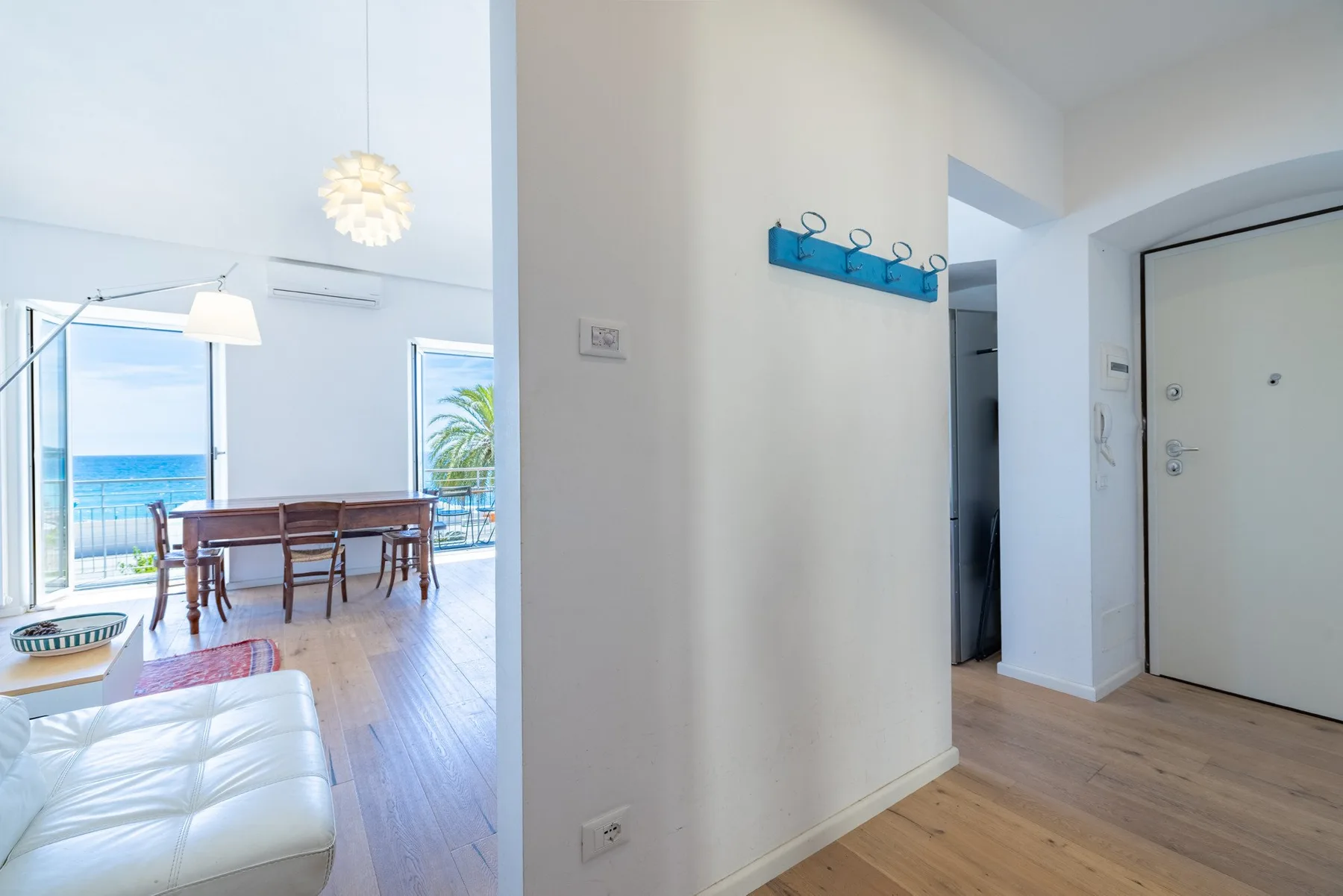 A bright apartment interior shows an entry hall opening into a dining area by the window.
