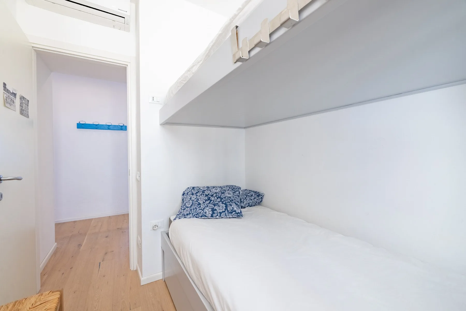 A compact bedroom with a single bed beneath a built-in overhead shelf.