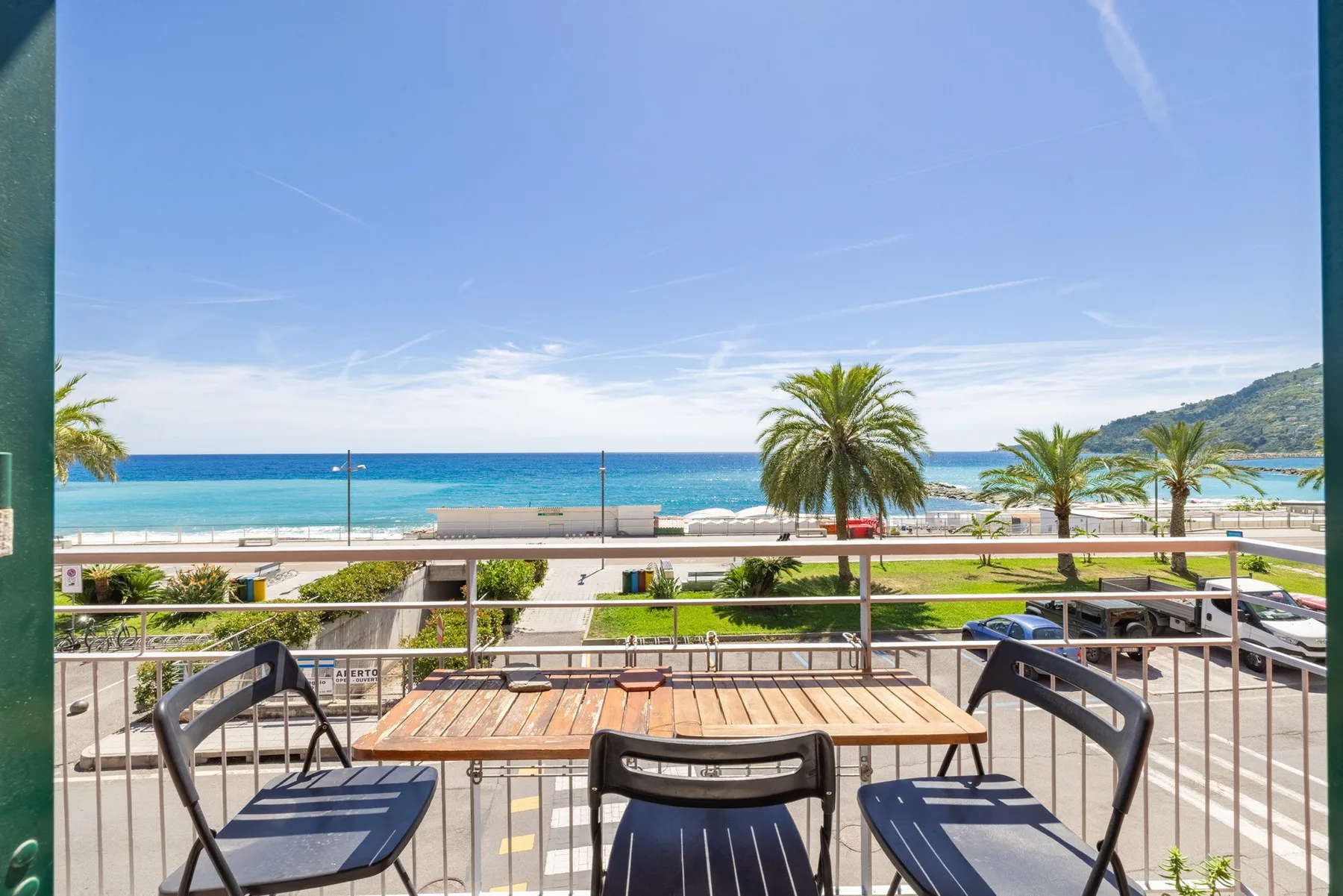 A balcony dining area overlooks the seaside promenade and blue water.