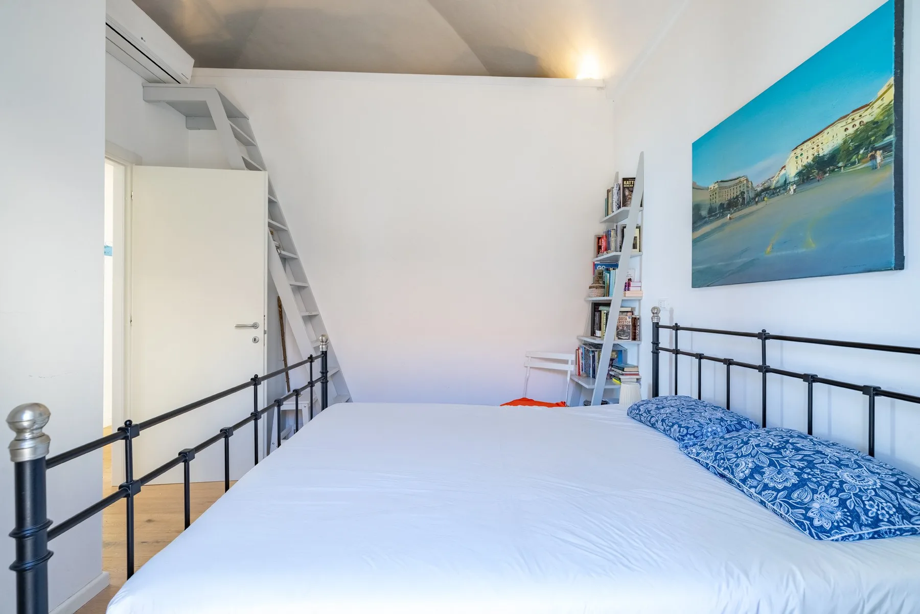 A bedroom with a bed, a ladder, and a colorful wall picture.