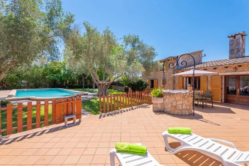 A sunny patio with lounge seating, a pool, and a stone house.
