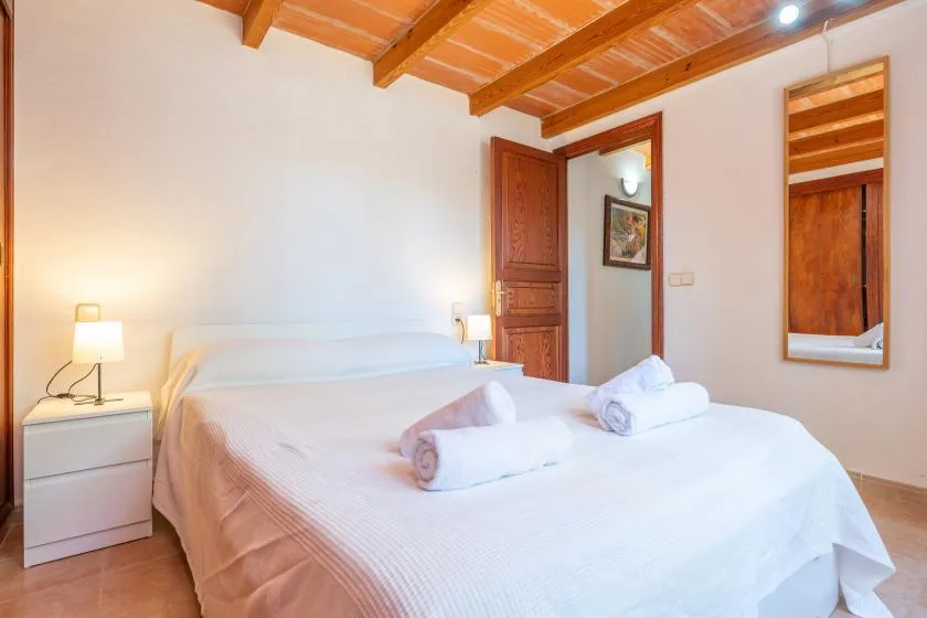 A bedroom with a large bed, bedside tables, and exposed wooden ceiling beams.