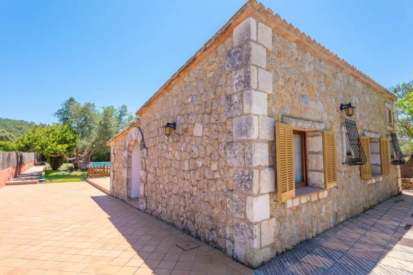 A stone house stands beside a sunlit paved courtyard.
