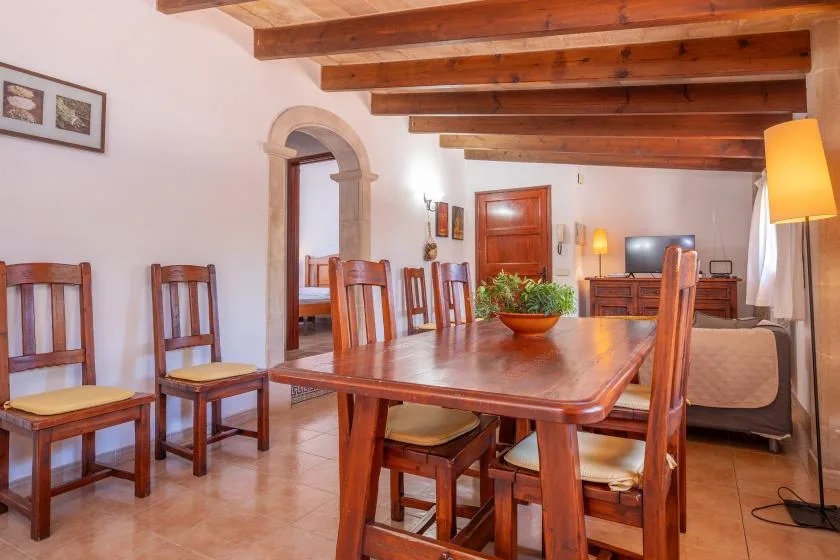 A dining area with a long wooden table and chairs beneath exposed ceiling beams.