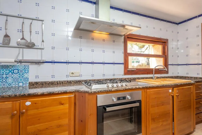 A tiled kitchen with wooden cabinetry, a cooktop, and an oven.