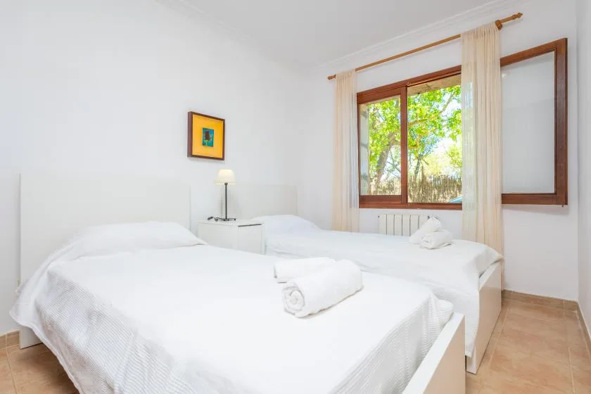 A bright bedroom with two beds beneath a large window.