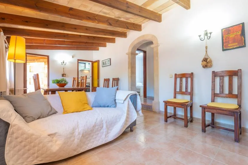 A bright living room has a daybed, wooden chairs, and exposed ceiling beams.