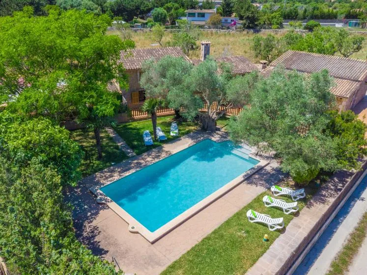 An outdoor swimming pool sits beside a tiled-roof building and leafy trees.