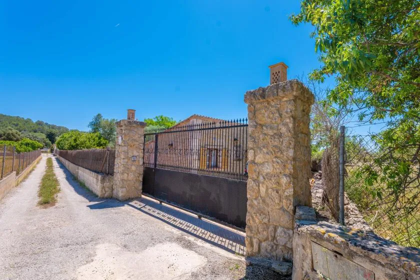 A gated property entrance with stone pillars, metal fencing, and a gravel driveway.
