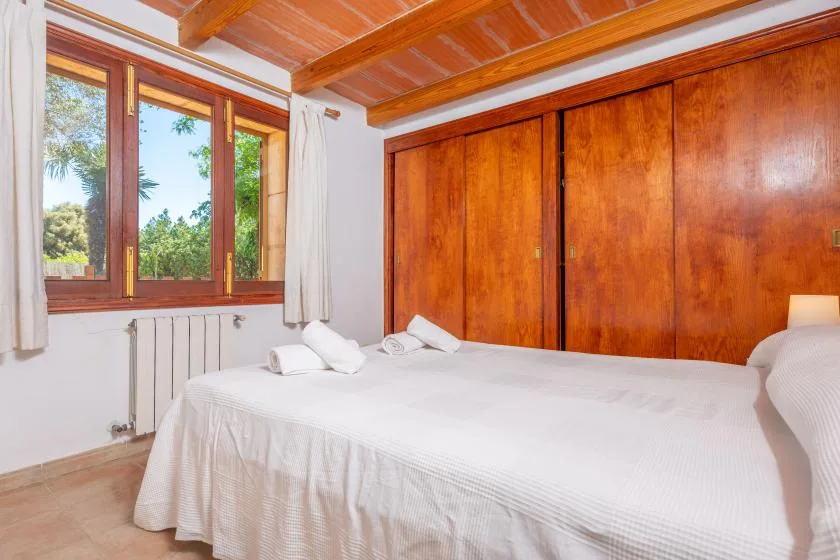 A bedroom with a bed beside a large window and wooden closets.