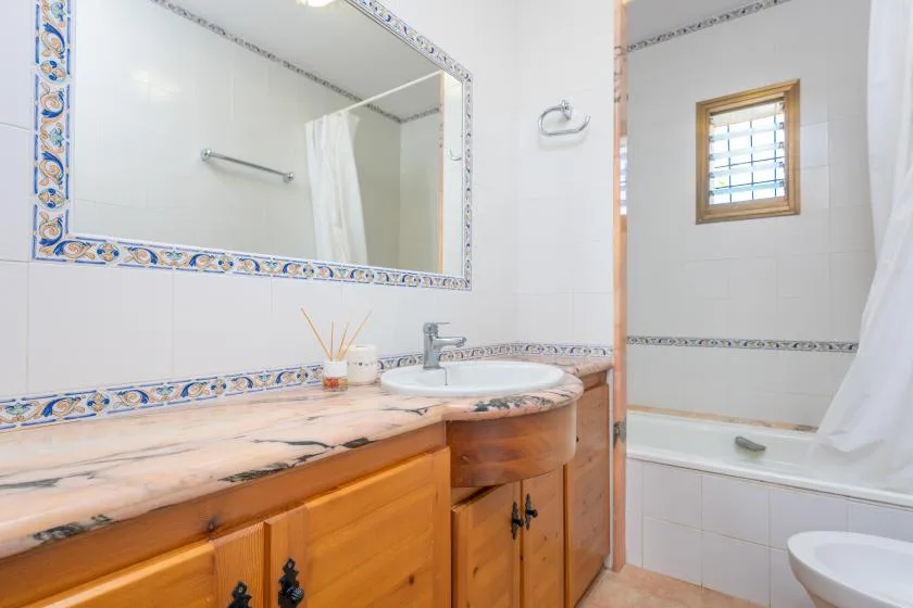 A tiled bathroom with a sink vanity, mirror, and bathtub.