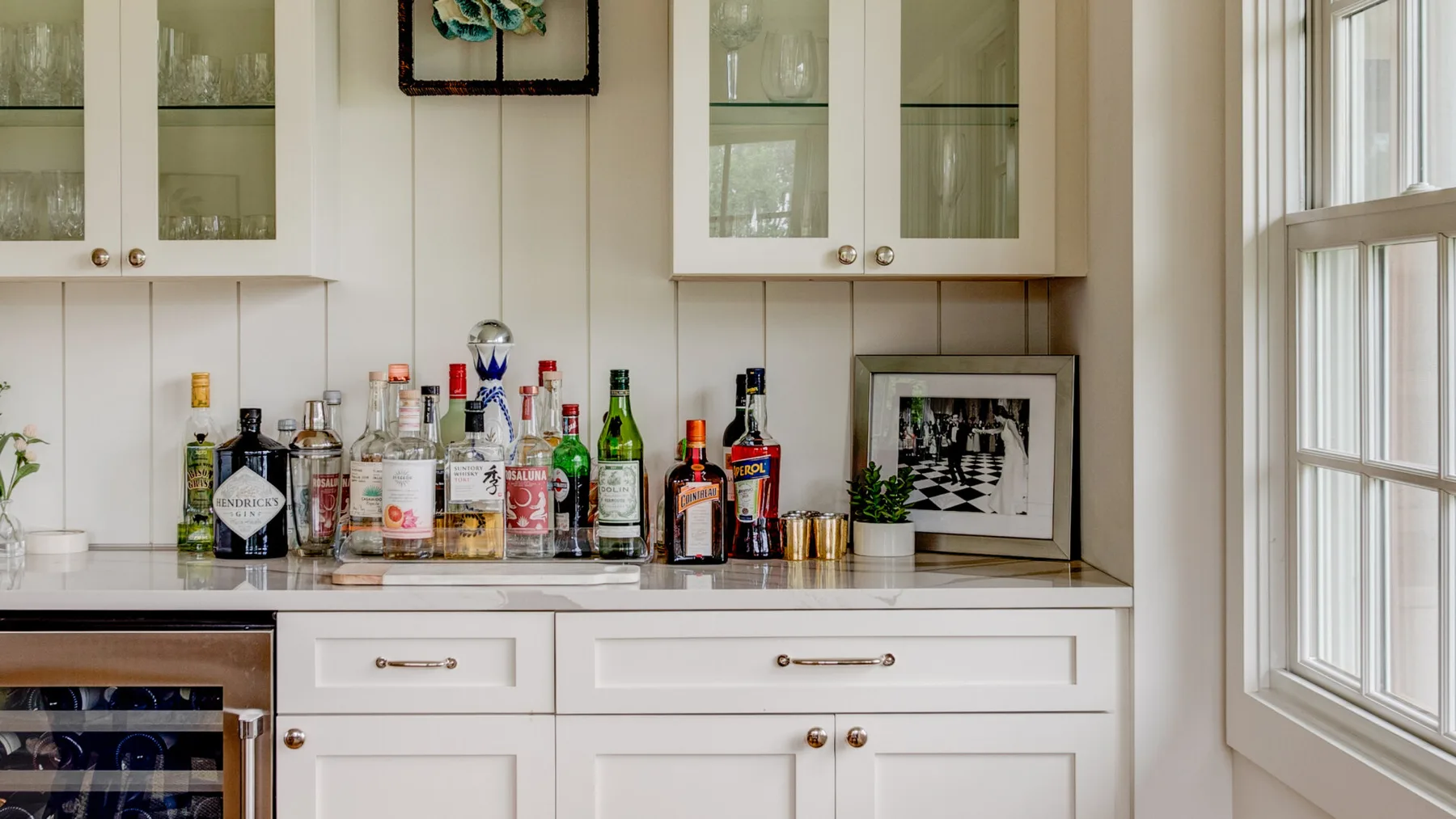 A bright built-in bar area with bottles arranged on a white countertop.